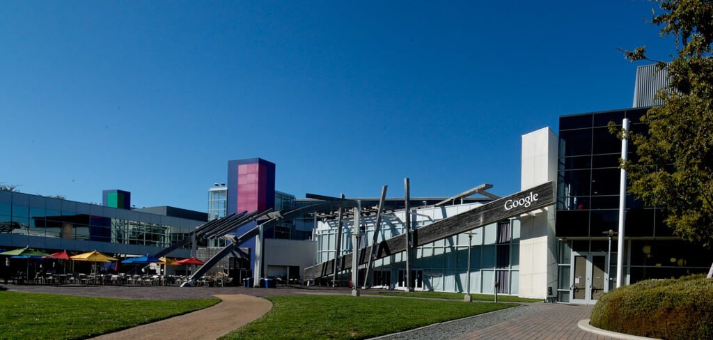 The Googleplex campus in Mountain View, California, with the Google logo mounted on a wooden beam above the entrance.