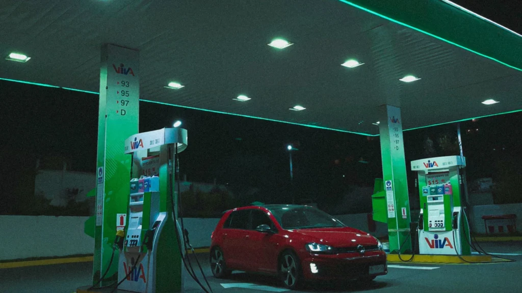 A red Volkswagen Golf parked at a gas station under bright neon lights at night