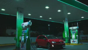 A red Volkswagen Golf parked at a gas station under bright neon lights at night