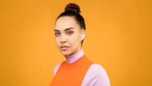 Portrait of a young woman wearing wireless earbuds against a vibrant orange background