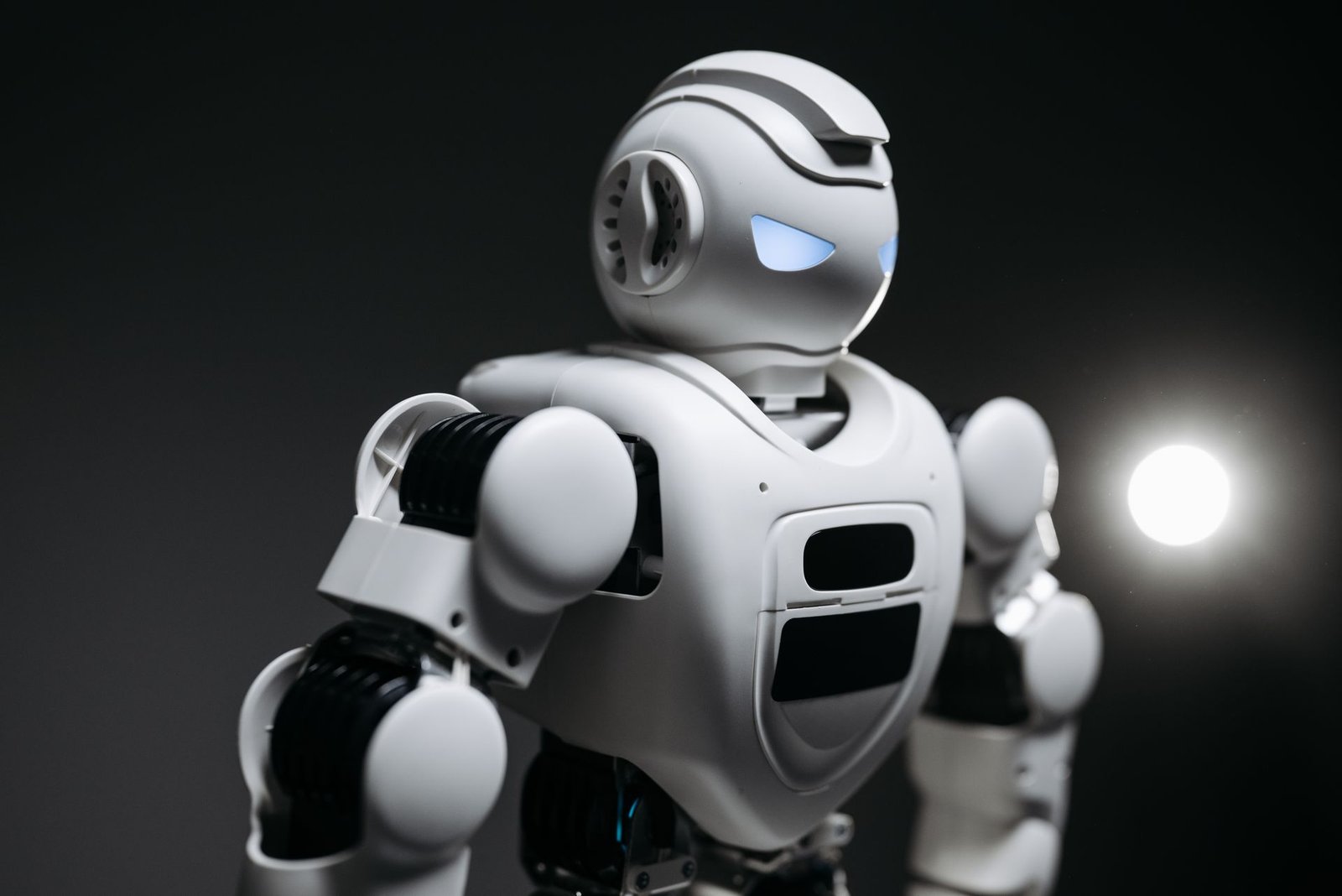 Close-up studio photograph of a white humanoid robot with glowing blue eyes against a black background