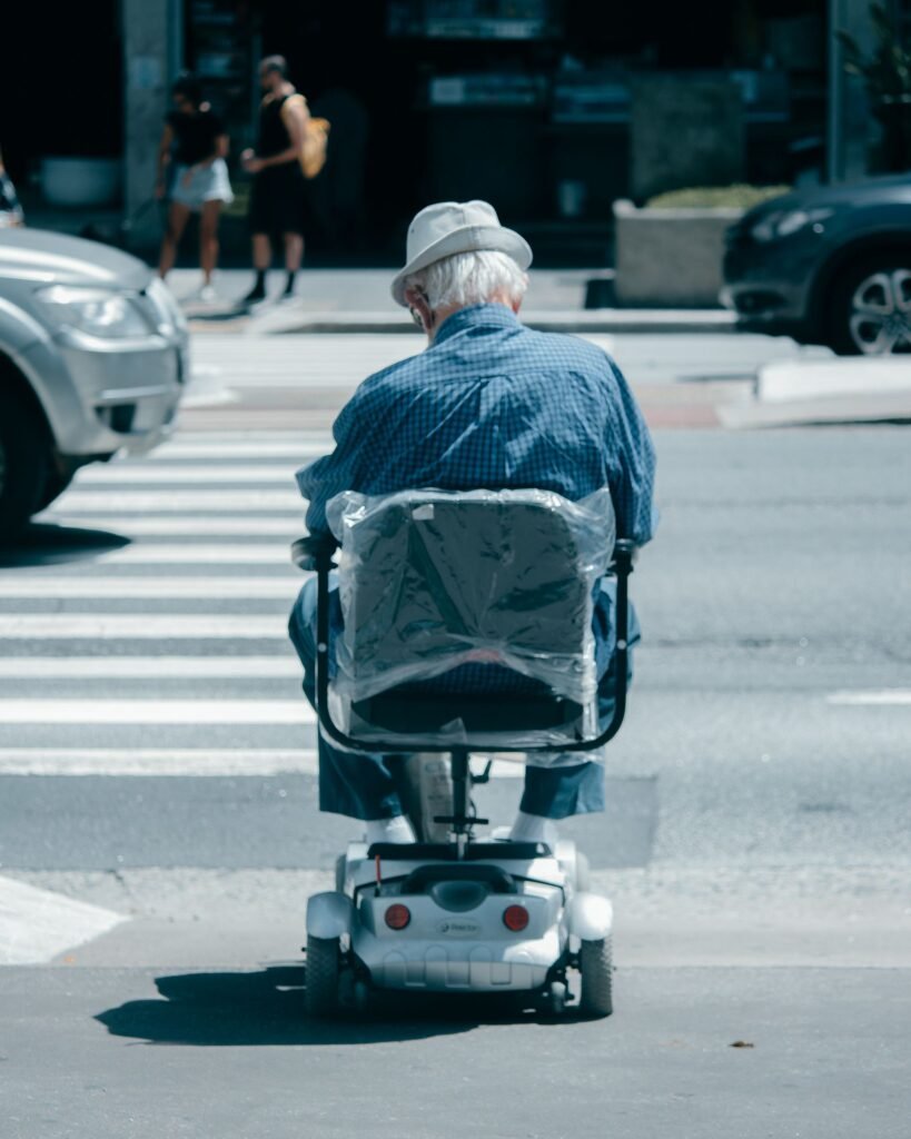 An elderly man navigating a city crosswalk in a modern electric wheelchair on a sunny day
