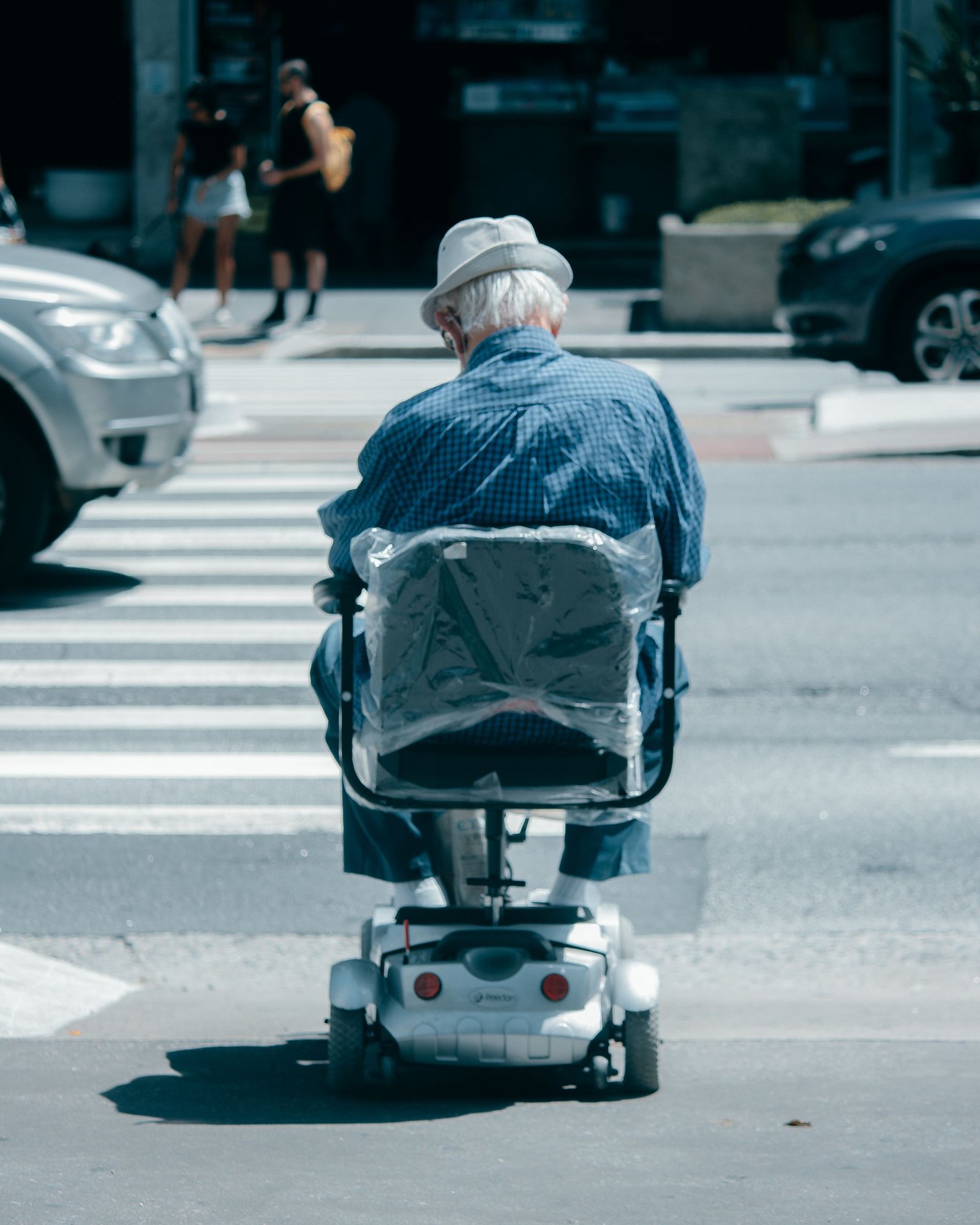 An elderly man navigating a city crosswalk in a modern electric wheelchair on a sunny day
