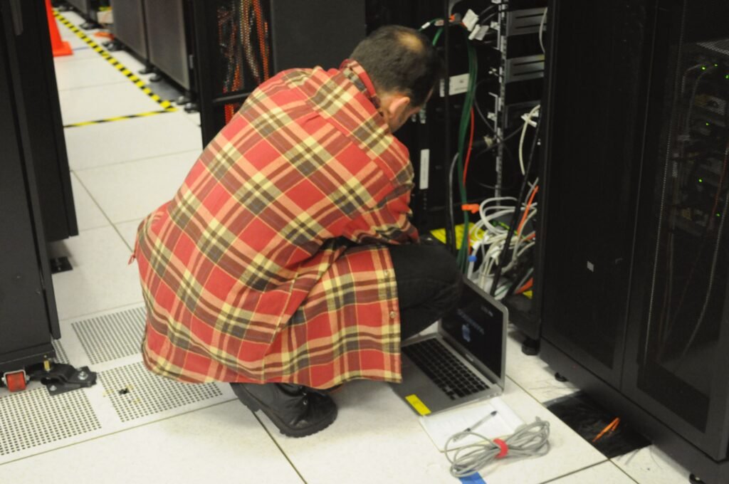 IT technician working on a laptop beside illuminated server racks in a data center