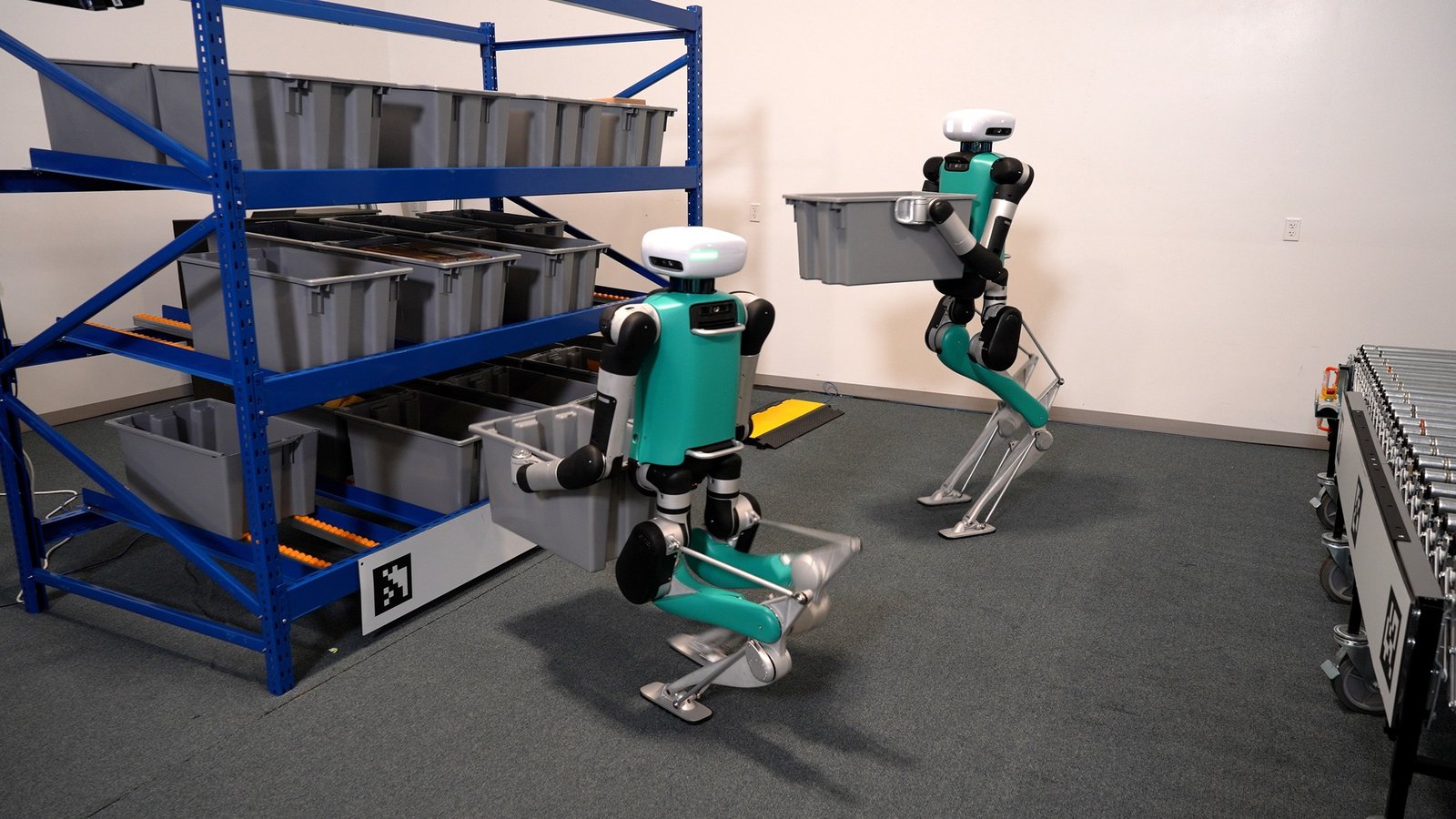 Two Agility Robotics Digit robots carrying totes in a warehouse