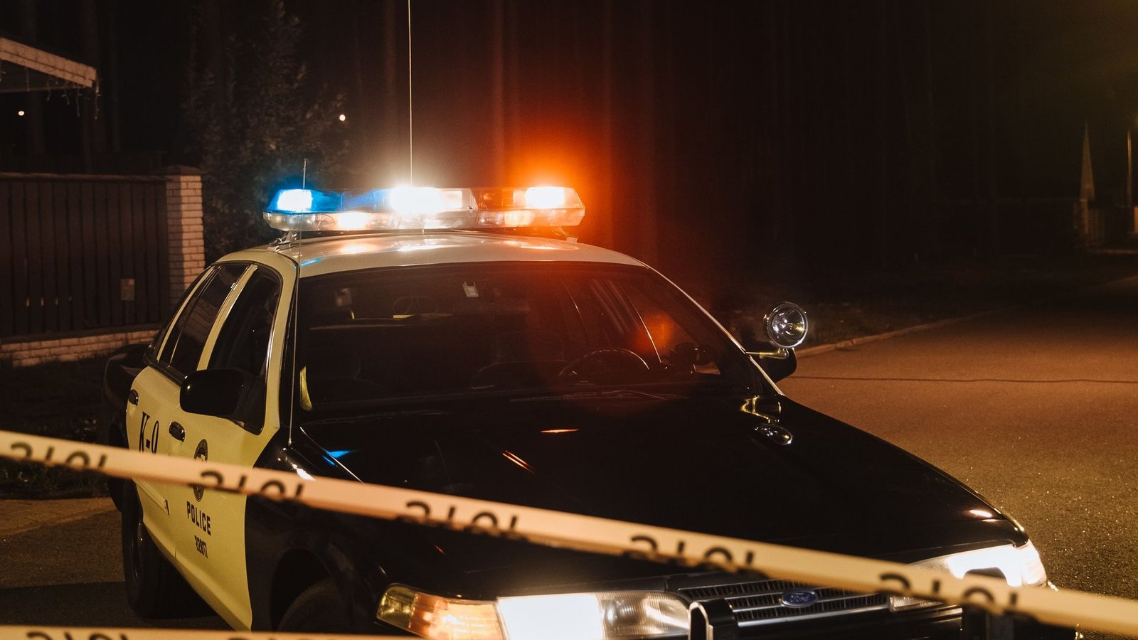 Police car with flashing red and blue lights behind crime-scene tape at night