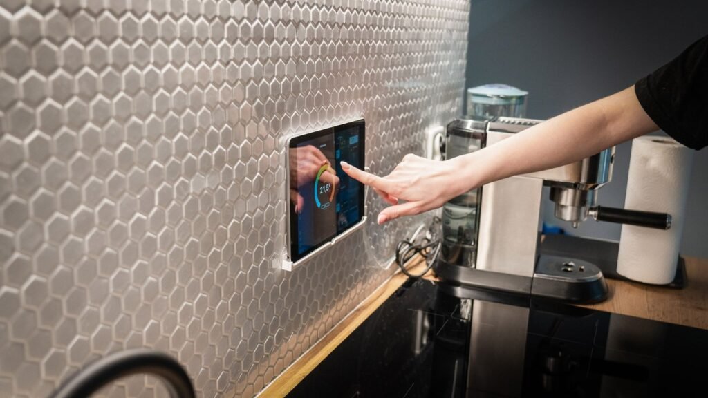 A hand touching a wall-mounted smart home touchscreen display in a modern kitchen