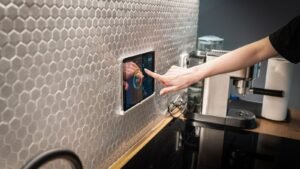 A hand touching a wall-mounted smart home touchscreen display in a modern kitchen