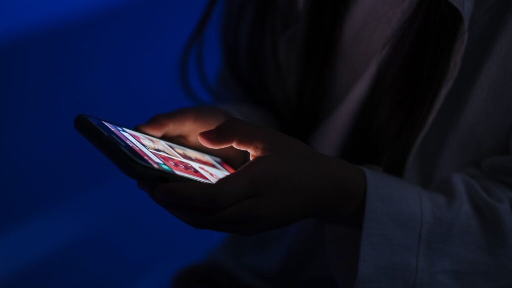A person using a smartphone in a dark room, the glowing screen lighting their hands