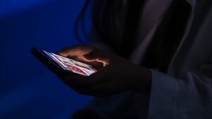 A person using a smartphone in a dark room, the glowing screen lighting their hands