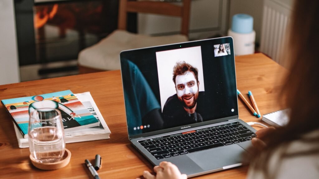Woman on a video call on a MacBook Pro at a wooden desk with a notebook and glass of water