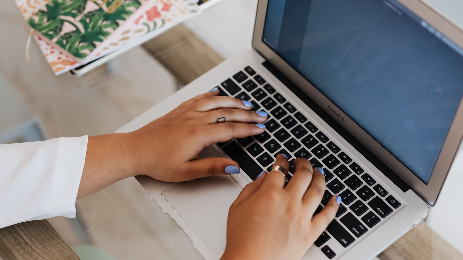 A person's hands typing on a laptop keyboard next to notebooks at a desk