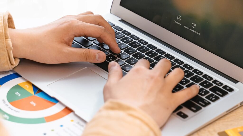 Person typing on a laptop with spreadsheet charts beside the keyboard