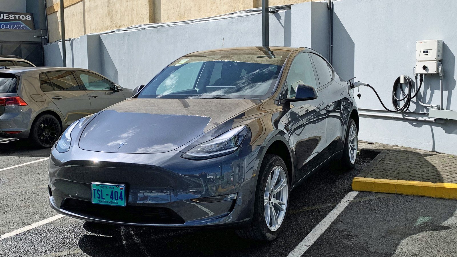 A dark gray Tesla Model Y plugged into a home wall charger with the charge cable connected