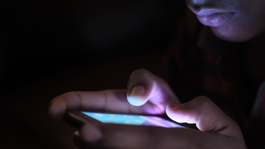 Hands holding a glowing smartphone in darkness