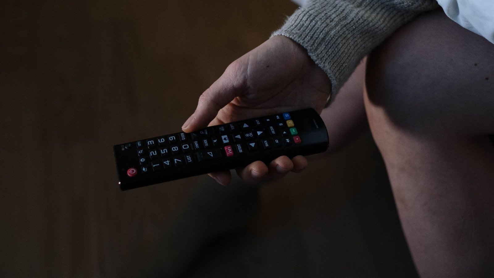 Hand holding a TV remote in a dimly lit room, taking back control of the screen