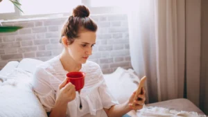 Woman holding a red coffee cup and reading her phone in bright morning light
