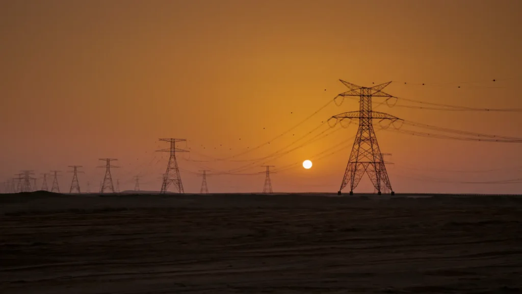 High-voltage transmission towers silhouetted against an orange sunset sky