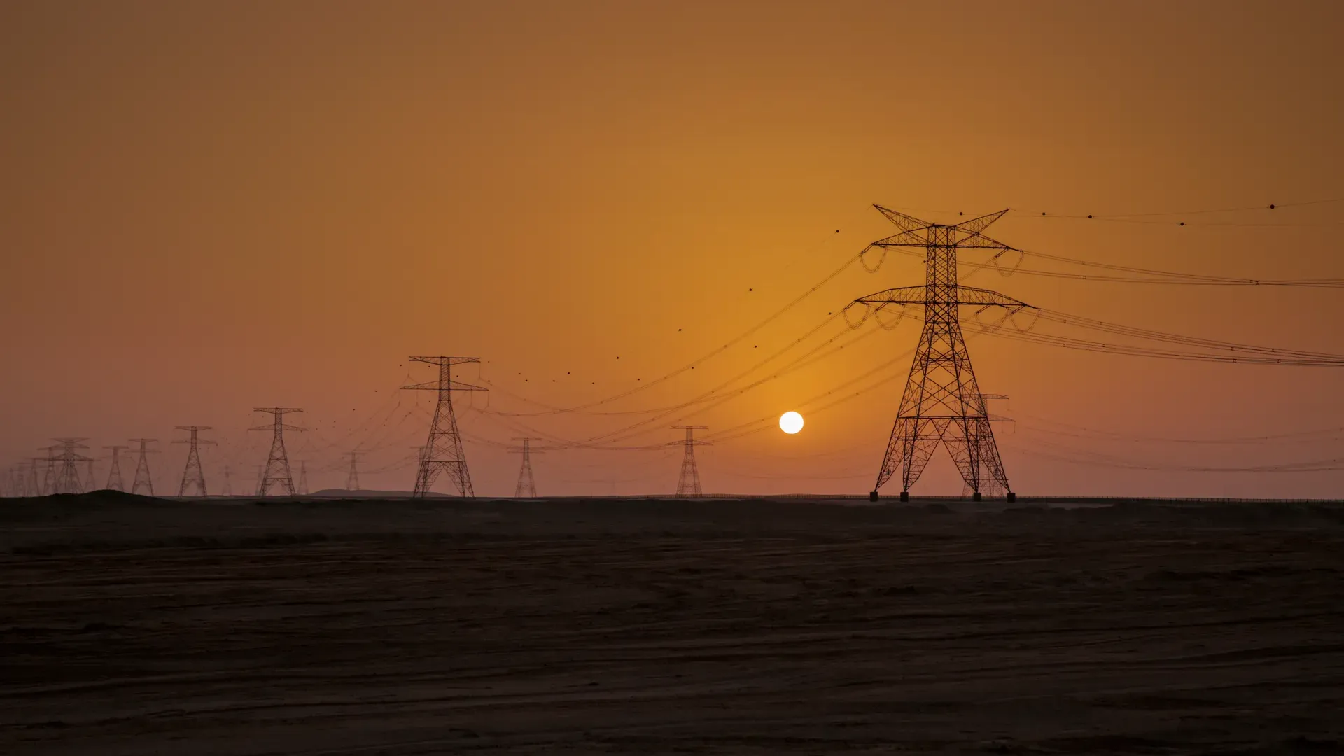 High-voltage transmission towers silhouetted against an orange sunset sky
