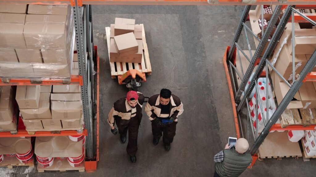 Overhead view of warehouse workers moving between tall shelves stacked with boxes and pallets