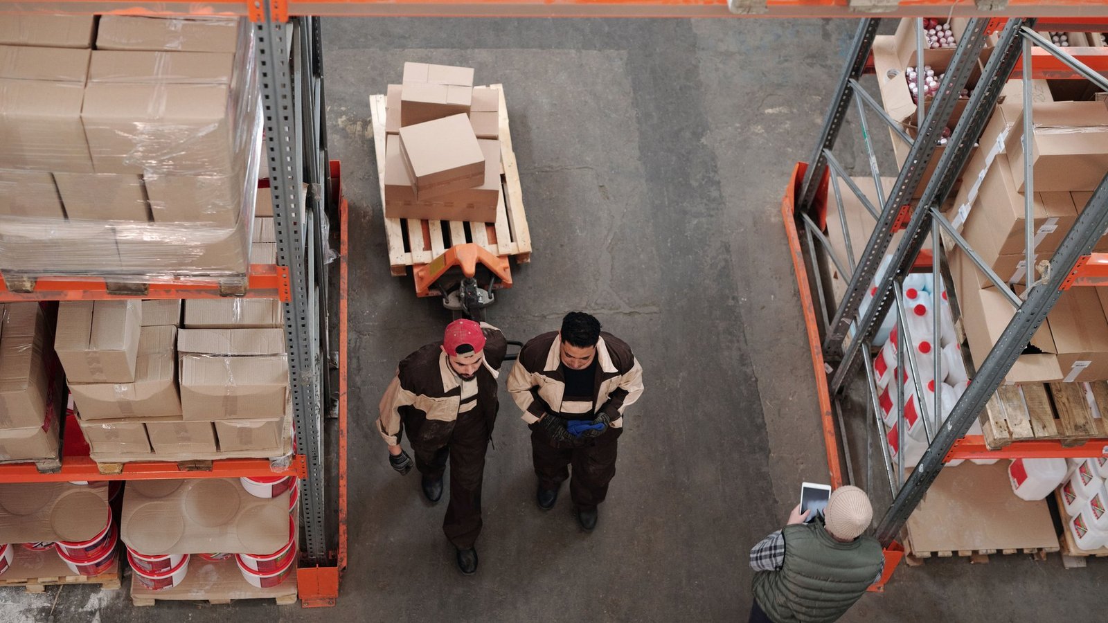 Overhead view of warehouse workers moving between tall shelves stacked with boxes and pallets