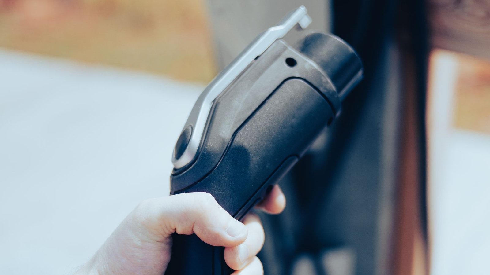 A hand gripping an EV fast-charging plug in front of a charging station