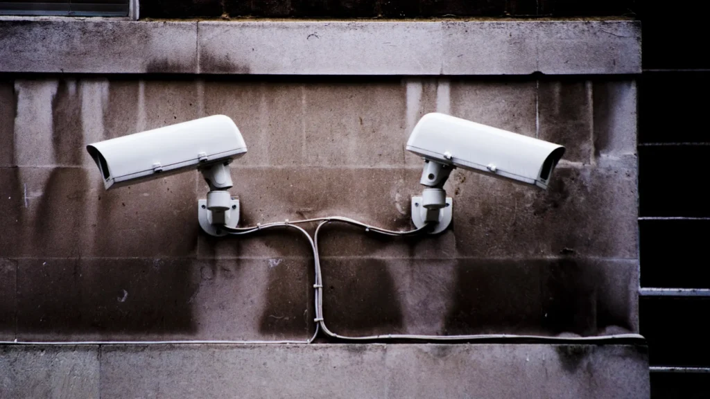 Two white CCTV surveillance cameras mounted on a concrete wall