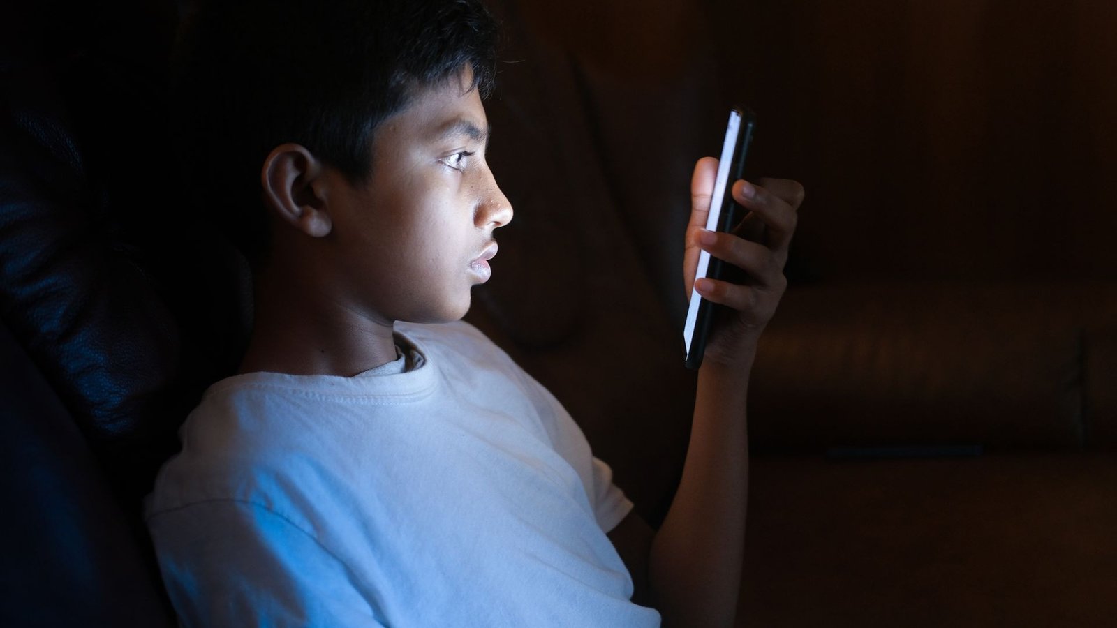 Young boy's face illuminated by a glowing smartphone screen in a dark room