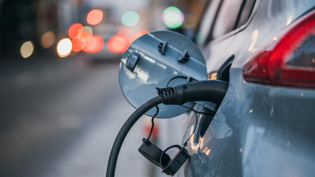 Close-up of an electric vehicle charging cable plugged into a car at dusk with city lights blurred behind it