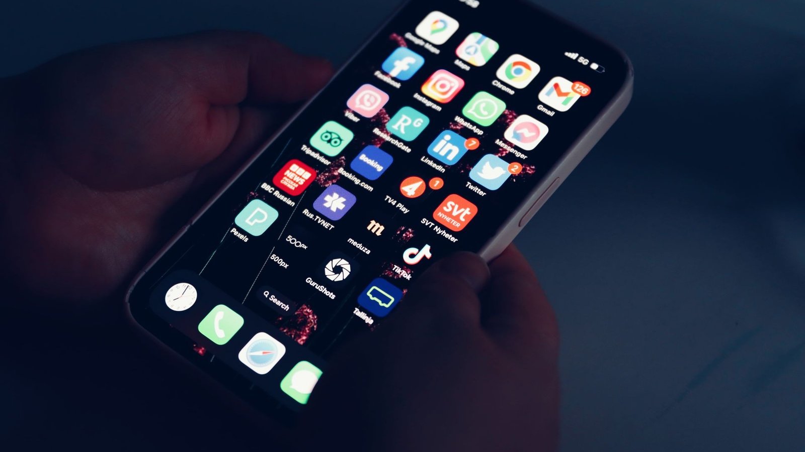 Close-up of a hand holding a smartphone with glowing app icons on screen in the dark