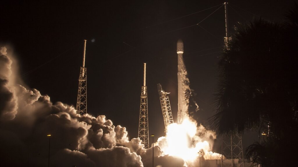A SpaceX Falcon 9 rocket lifting off at night with a bright engine plume and smoke billowing from the launch pad