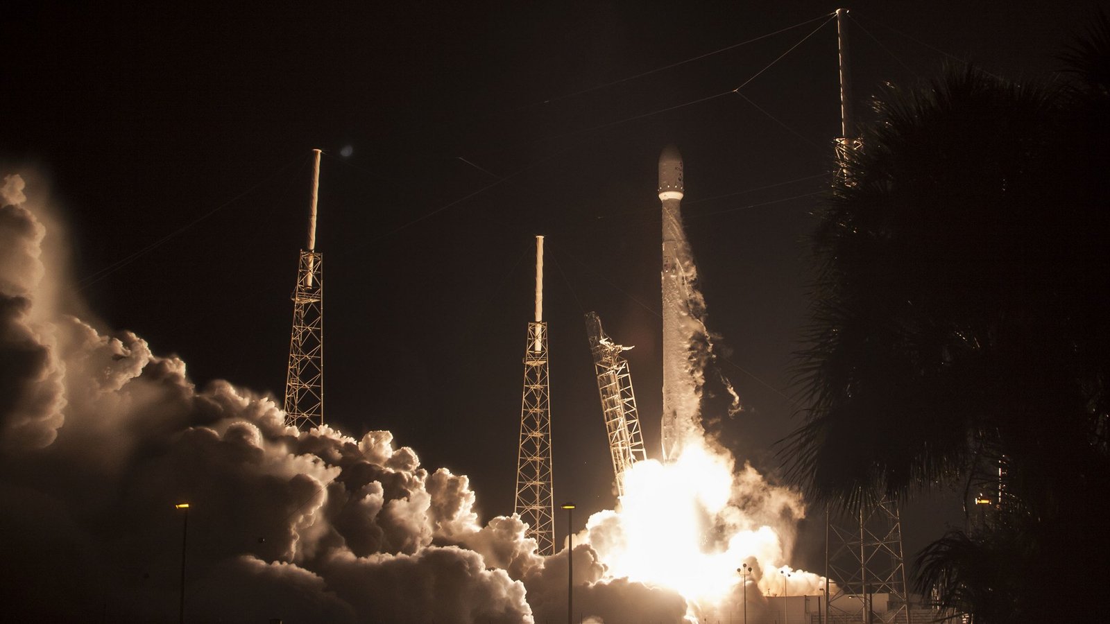 A SpaceX Falcon 9 rocket lifting off at night with a bright engine plume and smoke billowing from the launch pad