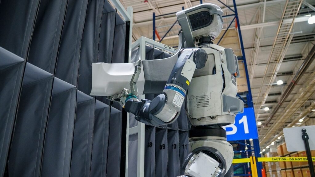 Boston Dynamics Atlas humanoid robot carrying a large box through a warehouse aisle