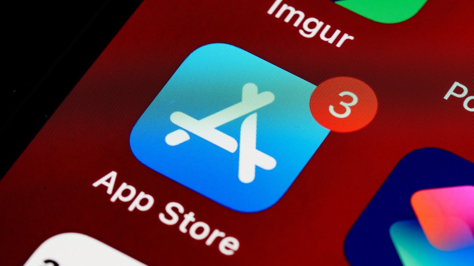 Close-up of the App Store icon on an iPhone screen against a deep red wallpaper