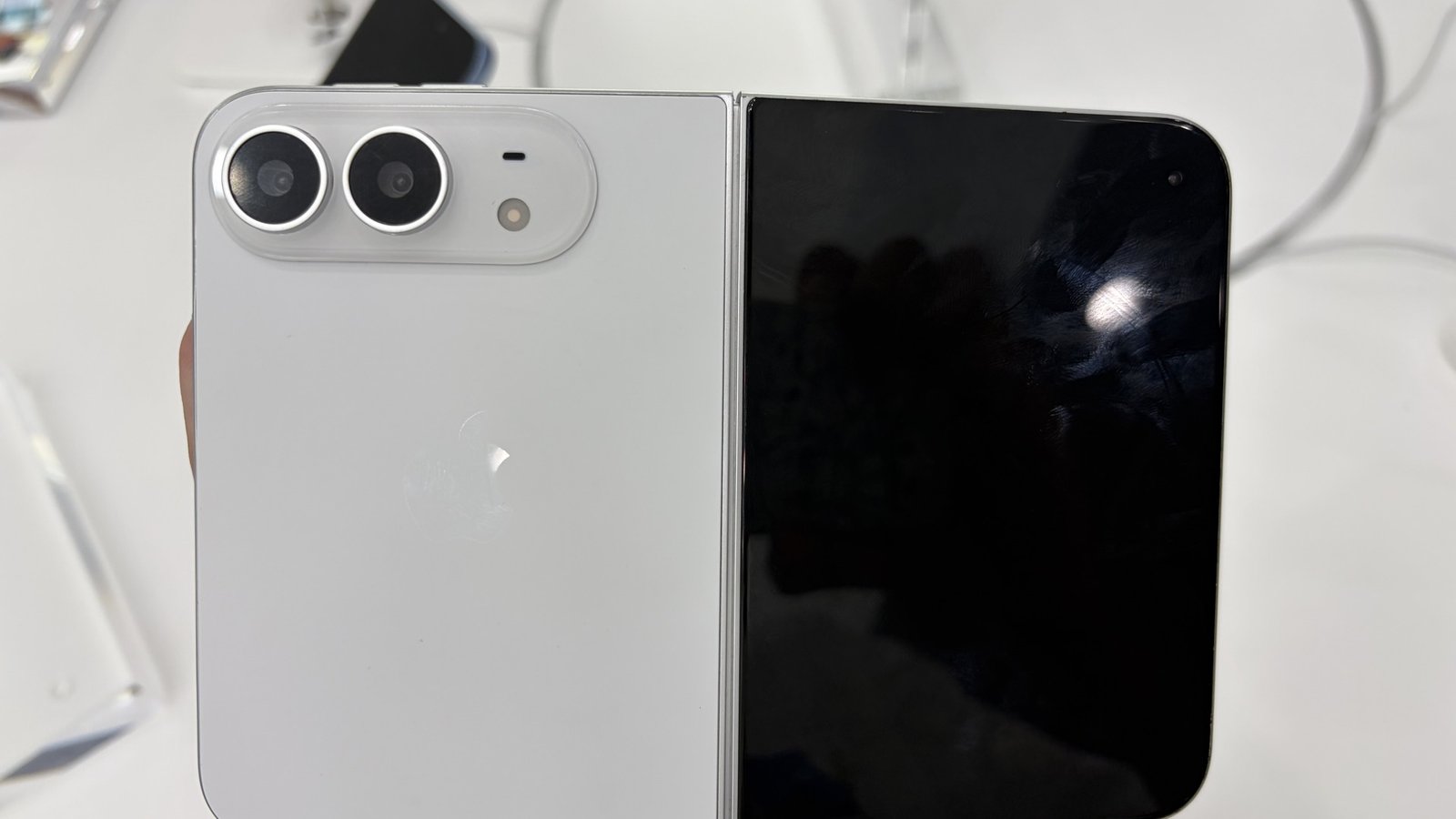 Unfolded white iPhone Duo held in a hand, showing the dual-camera plateau and Apple logo on the back