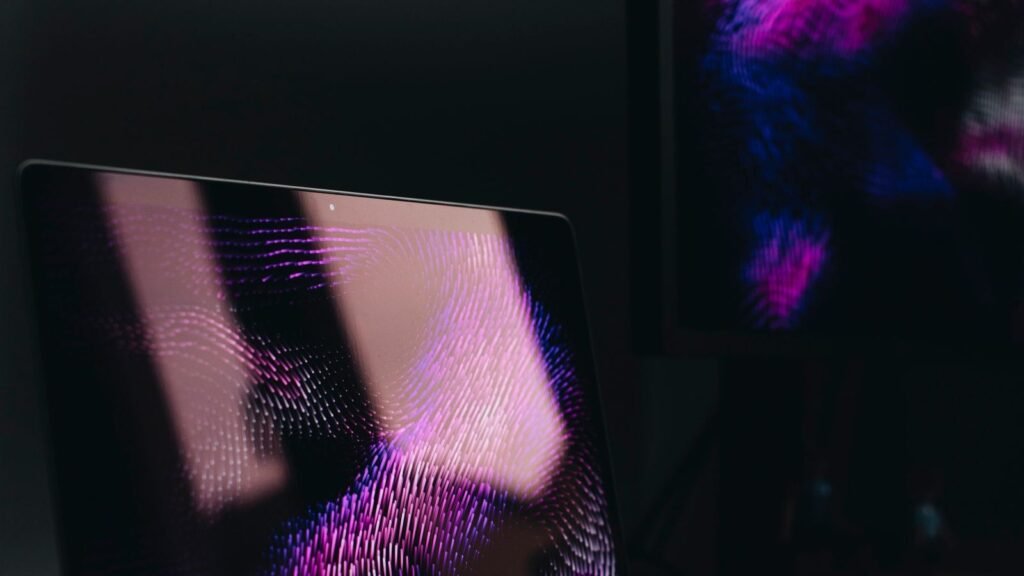 A MacBook Pro and external monitor glowing in a dark home office