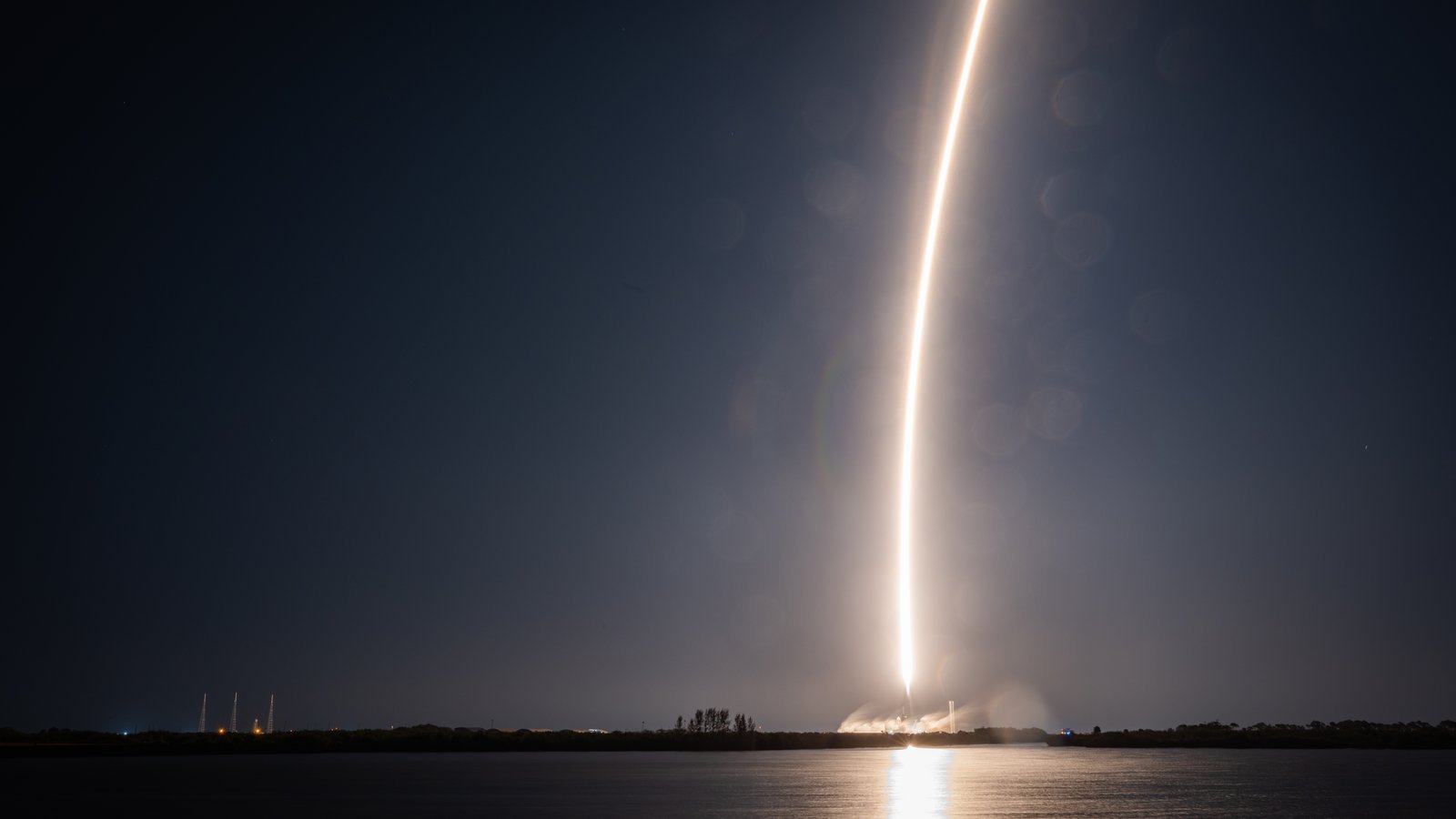A SpaceX Falcon 9 rocket arcs across the night sky in a long-exposure streak during liftoff