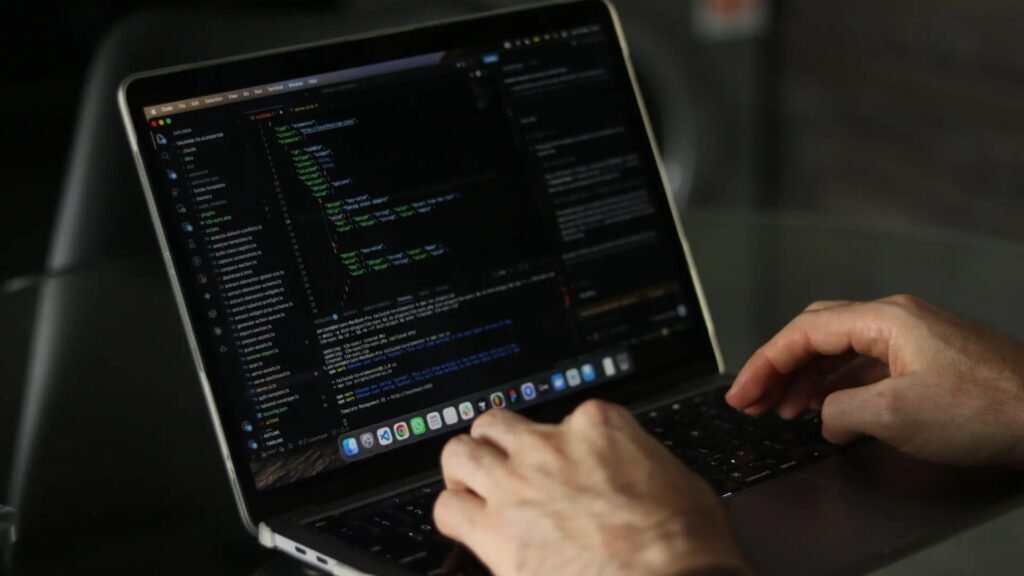 Close-up of a developer's hands typing code on a MacBook with a code editor on screen
