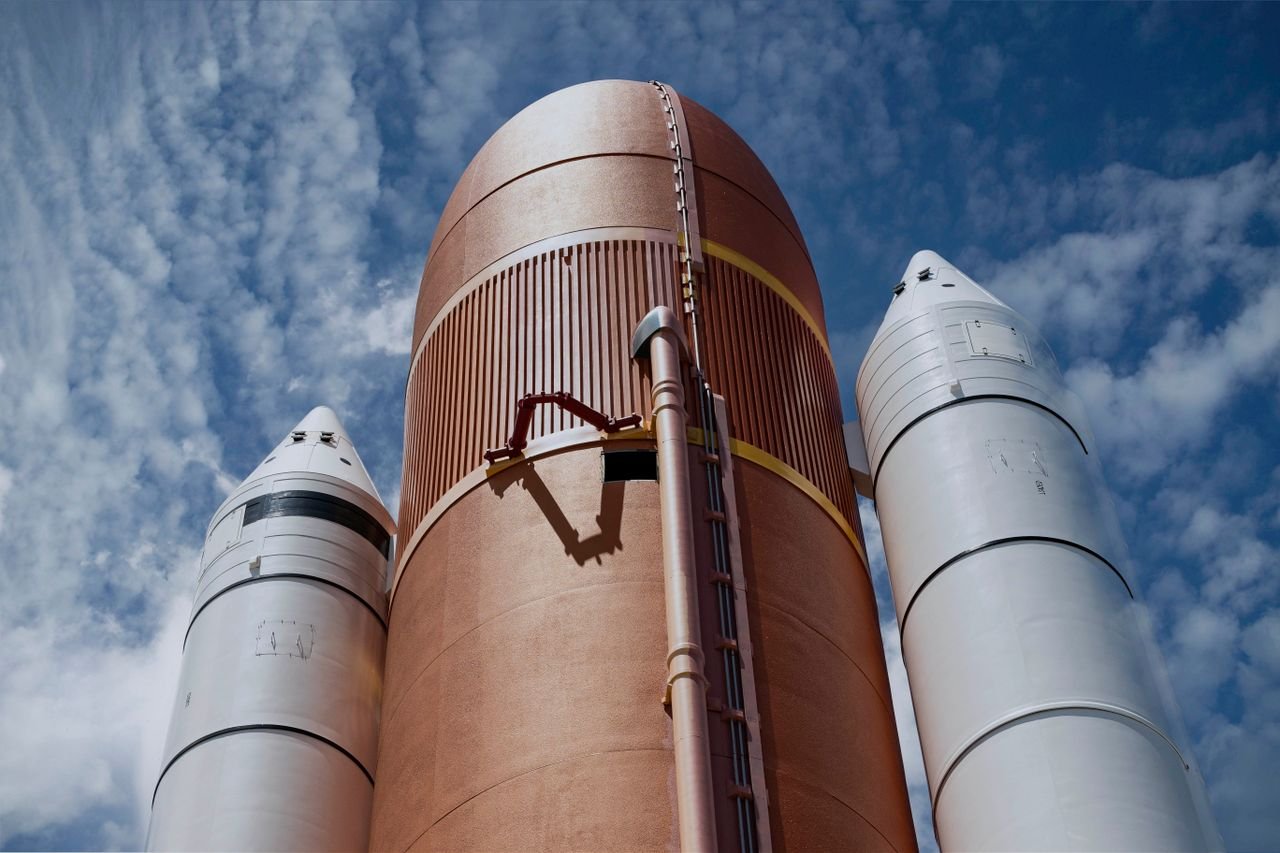 Orange rocket core stage standing between two white boosters against a blue sky.