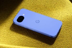 Google Pixel 10a smartphone in light blue lying on a textured yellow-green surface under dramatic side lighting