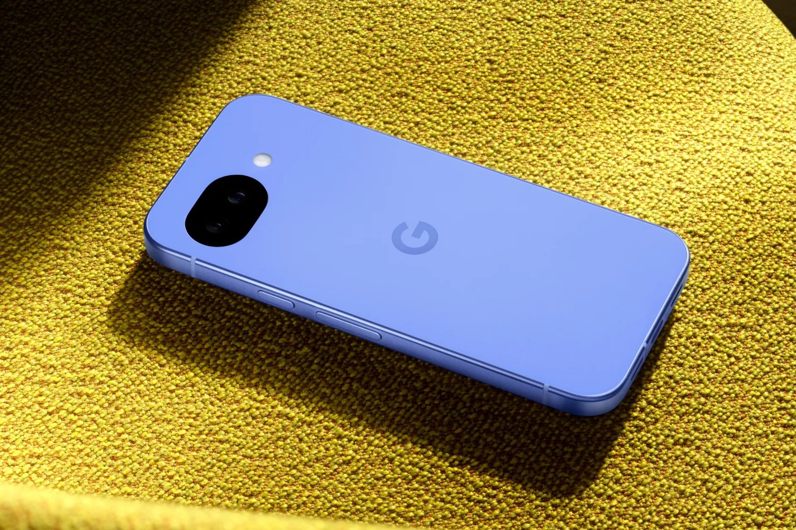 Google Pixel 10a smartphone in light blue lying on a textured yellow-green surface under dramatic side lighting