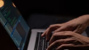 Hands typing on a laptop keyboard with code on screen in a dark room