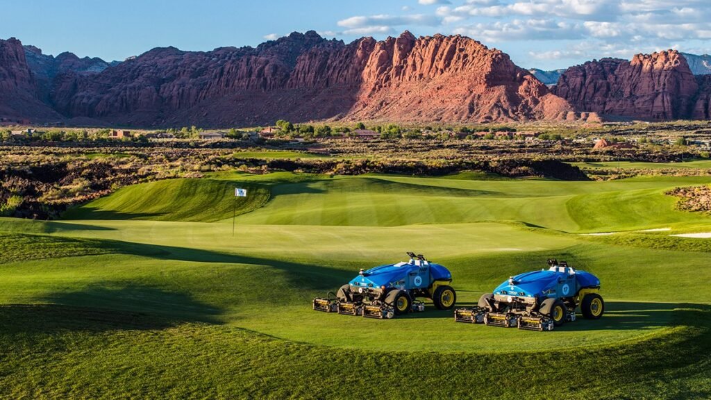 Two blue FireFly AMP autonomous mowers on a striped golf fairway at Black Desert Resort with red rock mountains behind them