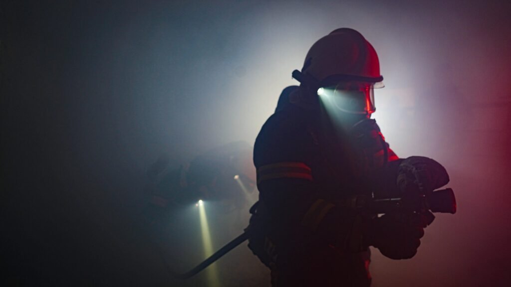 Firefighter in full gear with helmet flashlight moving through dense smoke
