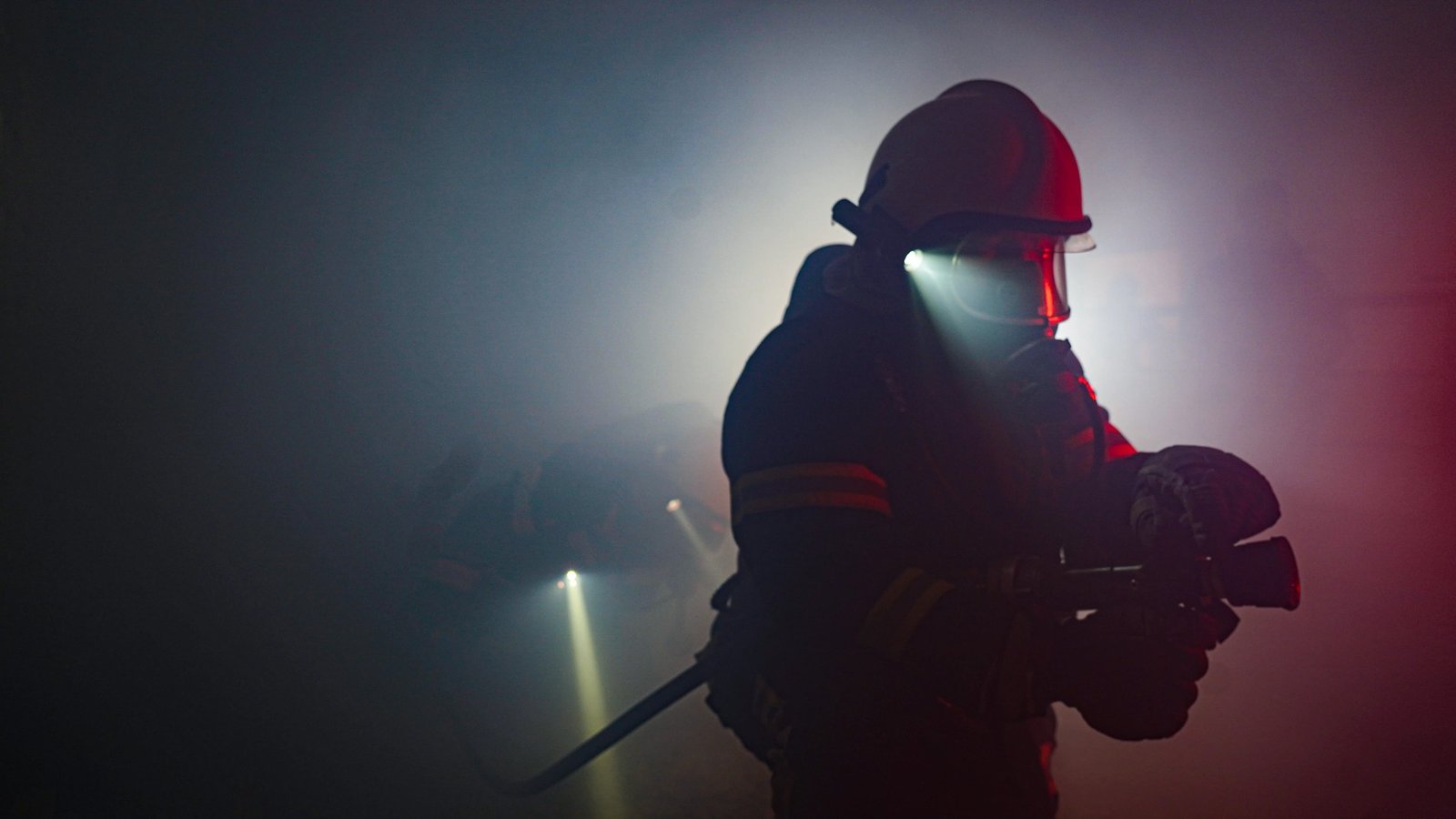 Firefighter in full gear with helmet flashlight moving through dense smoke