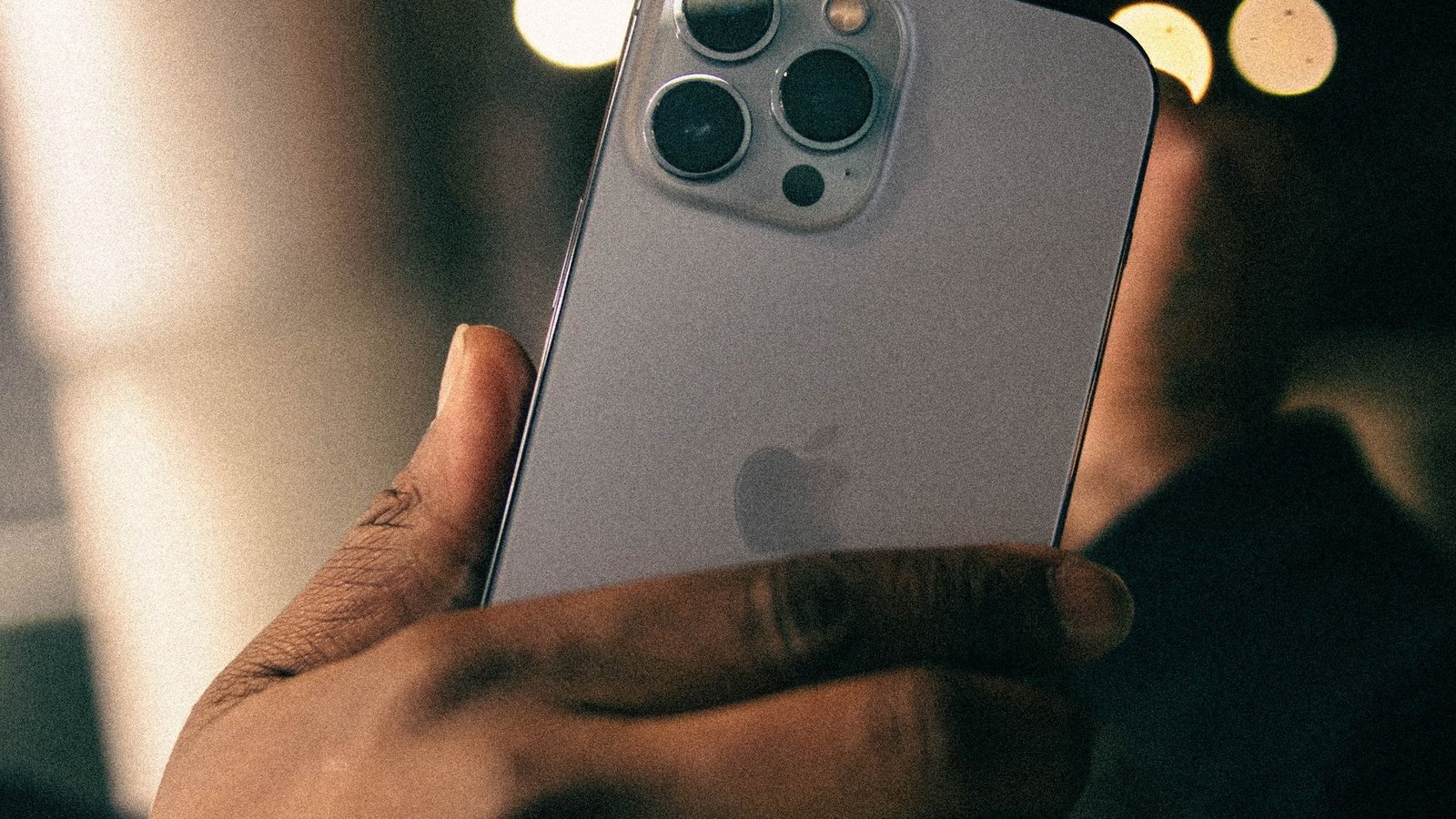 Hand holding an iPhone Pro with triple camera against night city lights