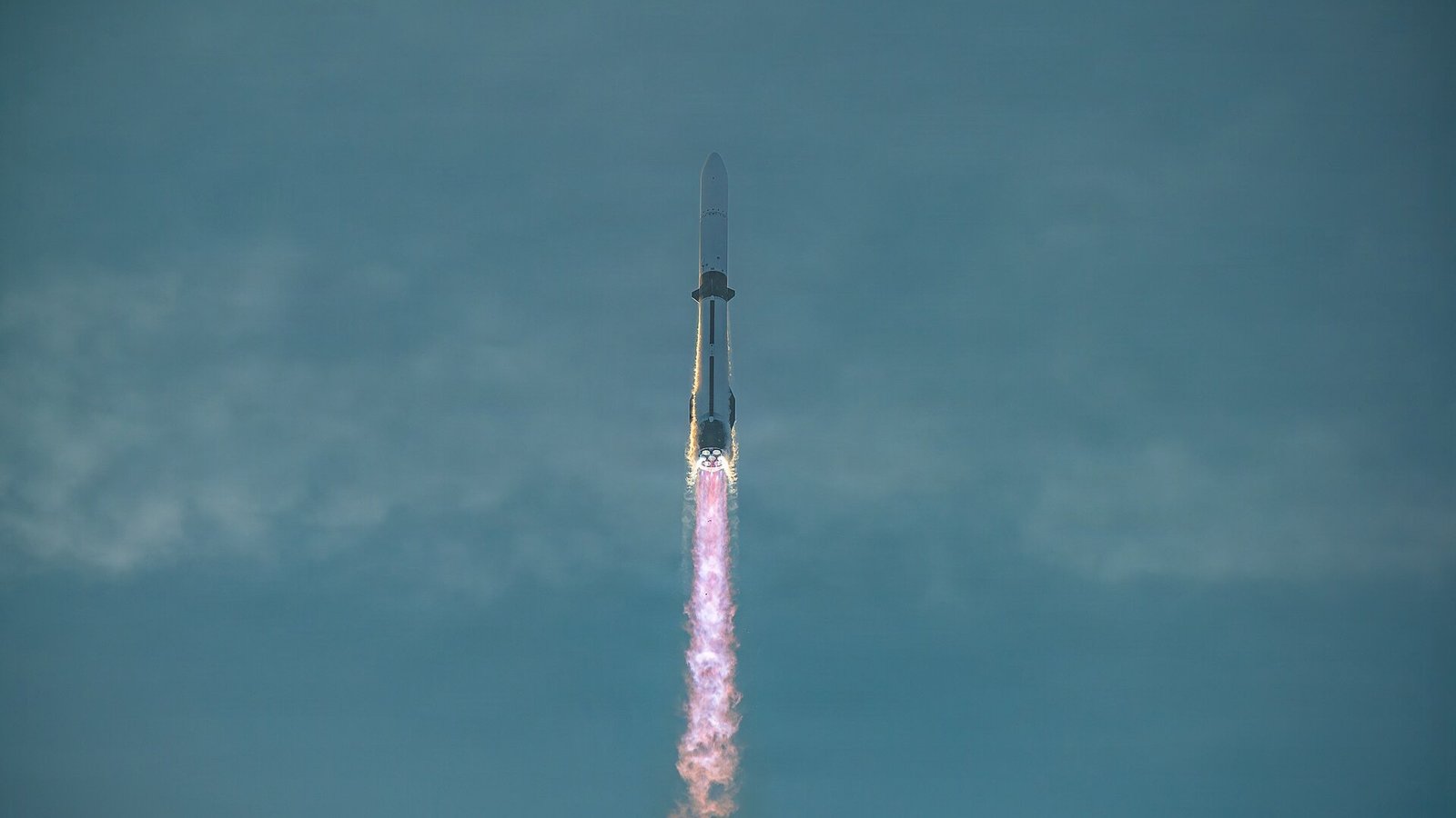 Blue Origin's New Glenn rocket ascending at dusk with its engines firing and a bright exhaust plume