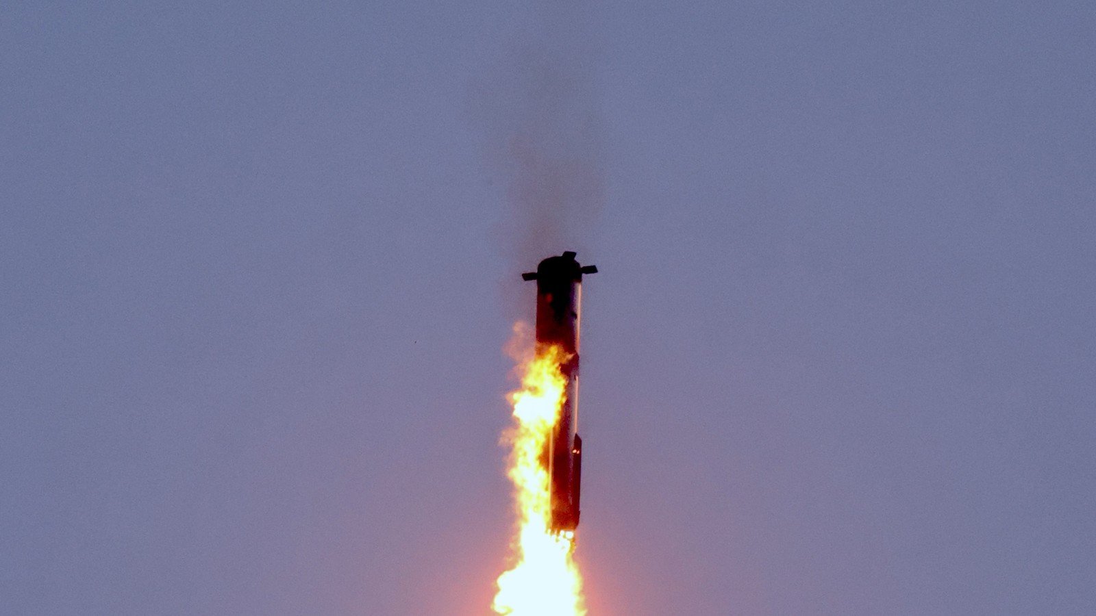 SpaceX Starship upper stage firing its engines during a landing burn beneath a dusk sky