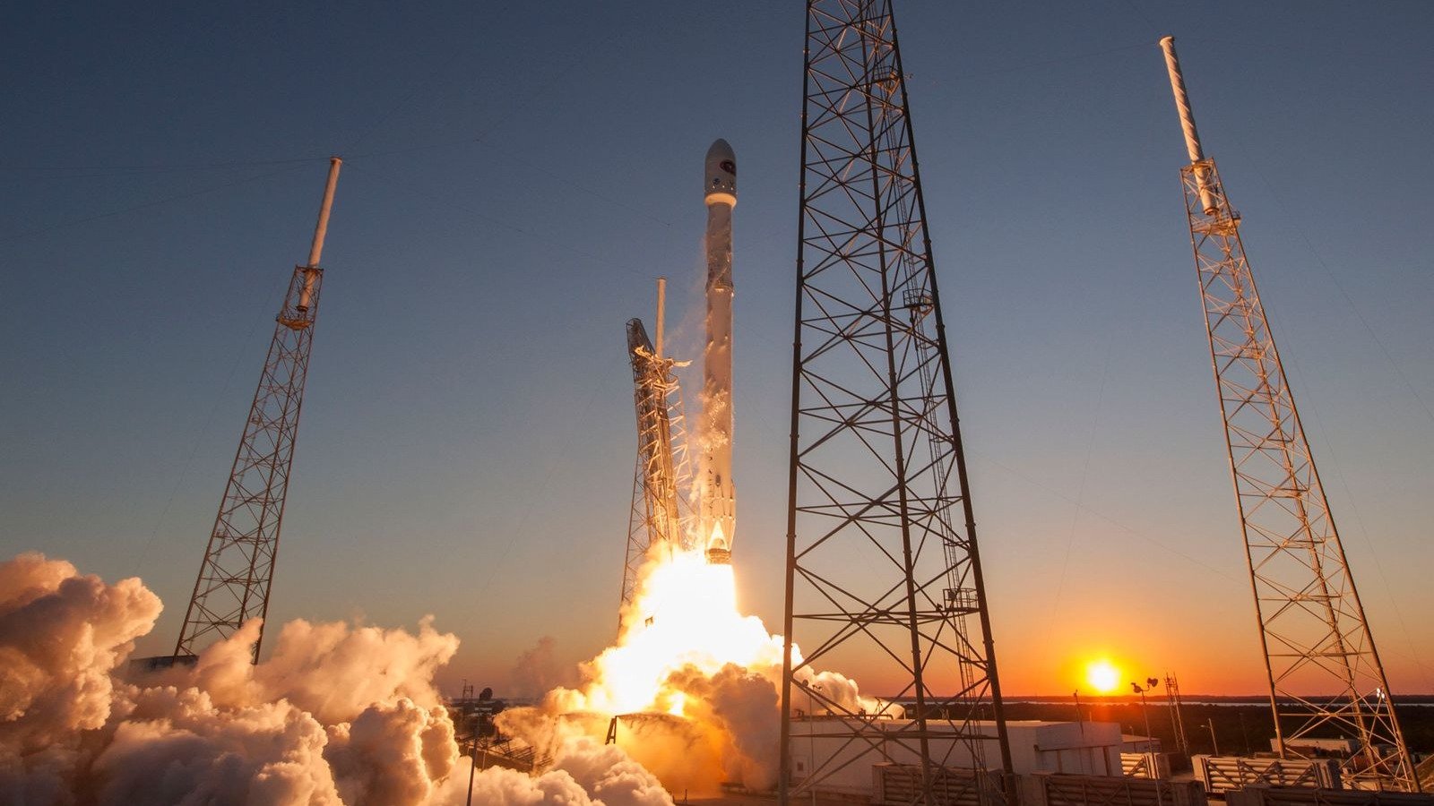 Falcon 9 rocket lifting off at sunset from launch towers at Cape Canaveral