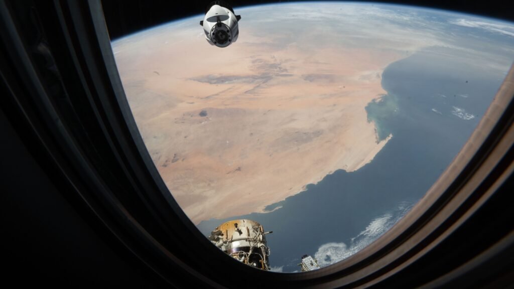 Cargo Dragon spacecraft seen through the ISS cupola window with Earth below during approach